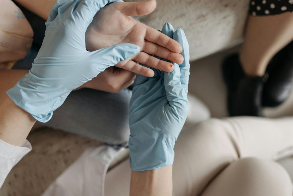 A medical professional wearing blue gloves examines a small wound on a person's finger indoors.