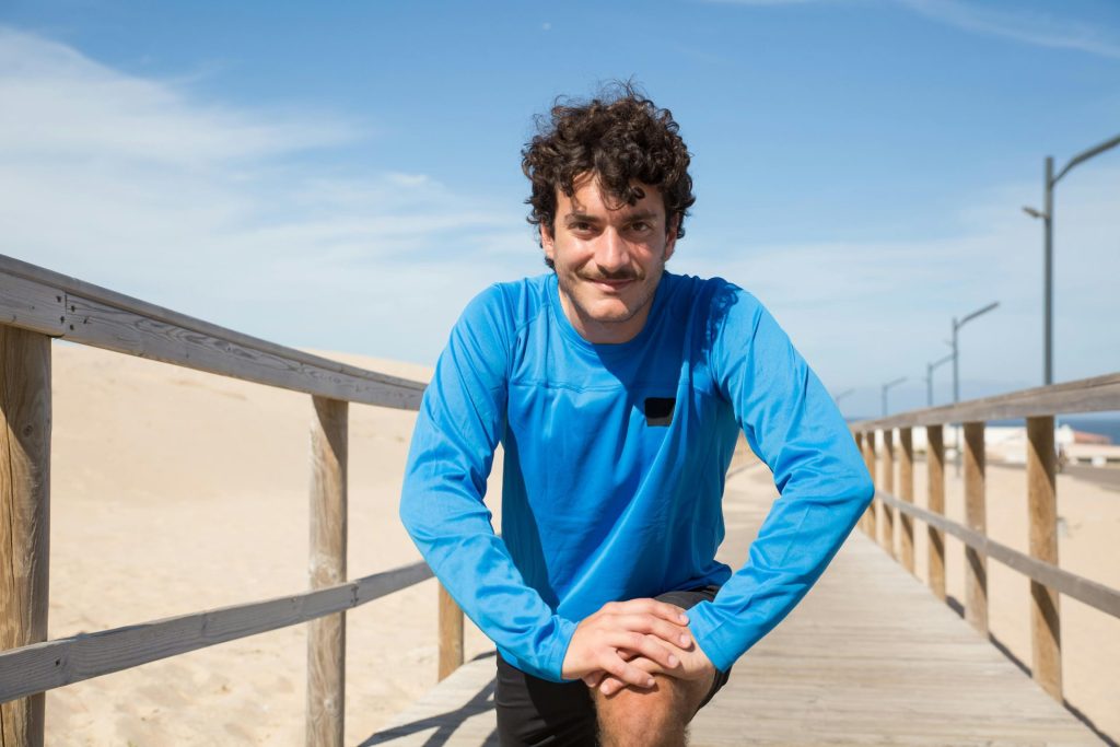 Adult man stretching on a scenic boardwalk by the sand dunes in Portugal, ideal for fitness themes.